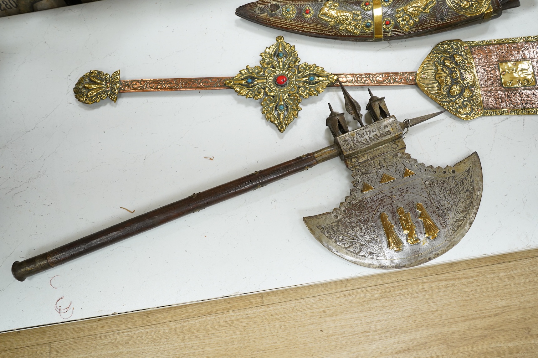 A decorative Indian axe, the large head inlaid with brass Hindu figures, together with a brass mounted North Indian kukri, another similar knife with bone handle, and a large shovel-shaped copper and brass item possibly